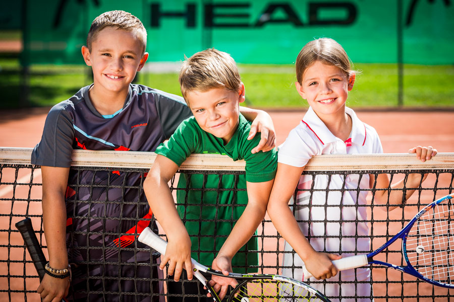 Juniors Tennis Kinder lehnen sich über Tennisnetz und halten ihre Schläger